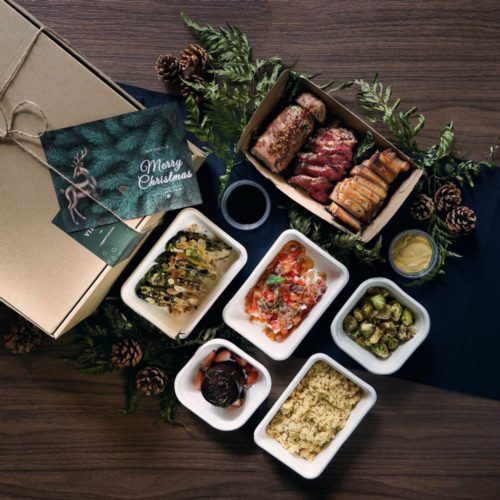 A food delivery box package from Botanico at The Garage with a spread of dishes from its Christmas 2020 2 Pax Menu ($98). Boxes and takeout containers hold Rump Cap, Kurobuta Pork Belly's or Turkey Bacon Roulade, and side dishes of "Chicken Rice" Couscous and a colourful burrata  and Palermo dish, as well as Chocolate Merlot Cake for dessert. 