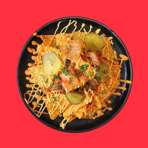 A plate of tortilla chips drizzled with cheese and topped with kimchi salsa, pickled cucumbers, and more. Nacho Kimcheese by Phat Fingers, with islandwide food delivery in Singapore powered by Oddle.